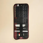 A black and burgundy artist pencil set in a roll-up canvas case, displayed against a solid beige background. The set includes various sizes of black graphite pencils, white tips, and drawing tools.