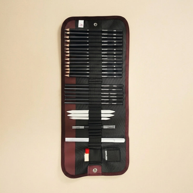 A black and burgundy artist pencil set in a roll-up canvas case, displayed against a solid beige background. The set includes various sizes of black graphite pencils, white tips, and drawing tools.