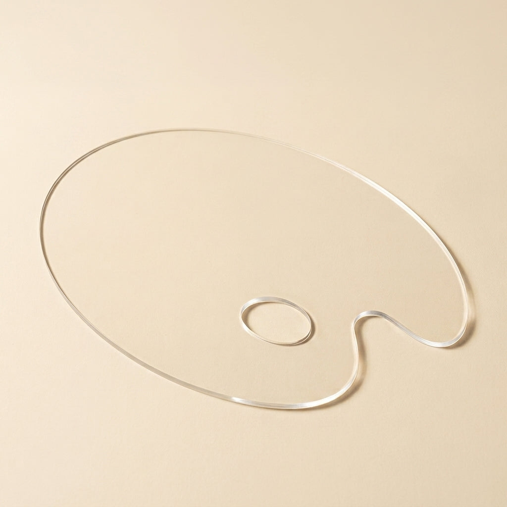 A clear acrylic artist palette-shaped object with a small loop, photographed on a warm beige background.