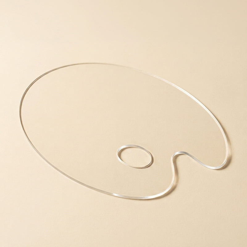 A clear acrylic artist palette-shaped object with a small loop, photographed on a warm beige background.