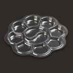 A clear plastic flower-shaped multi-compartment tray with a central oval well, photographed on a dark gray background.