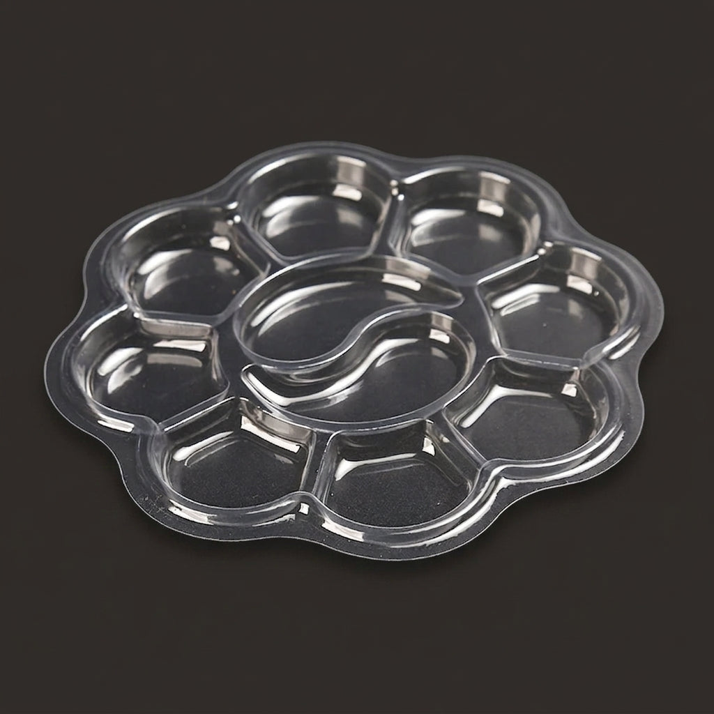 A clear plastic flower-shaped multi-compartment tray with a central oval well, photographed on a dark gray background.