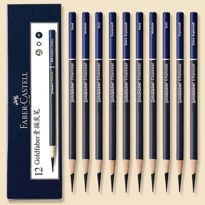 A set of 12 Faber-Castell Goldfaber charcoal pencils arranged next to their dark blue packaging box on a light beige background. The pencils have dark blue barrels with white text indicating different graphite grades (H, M, B, F, 2H, 2B, 3B, 4B, 5B, 6B, 7B, 8B, 9B, 10B, 12B) and are shown with their sharpened tips.