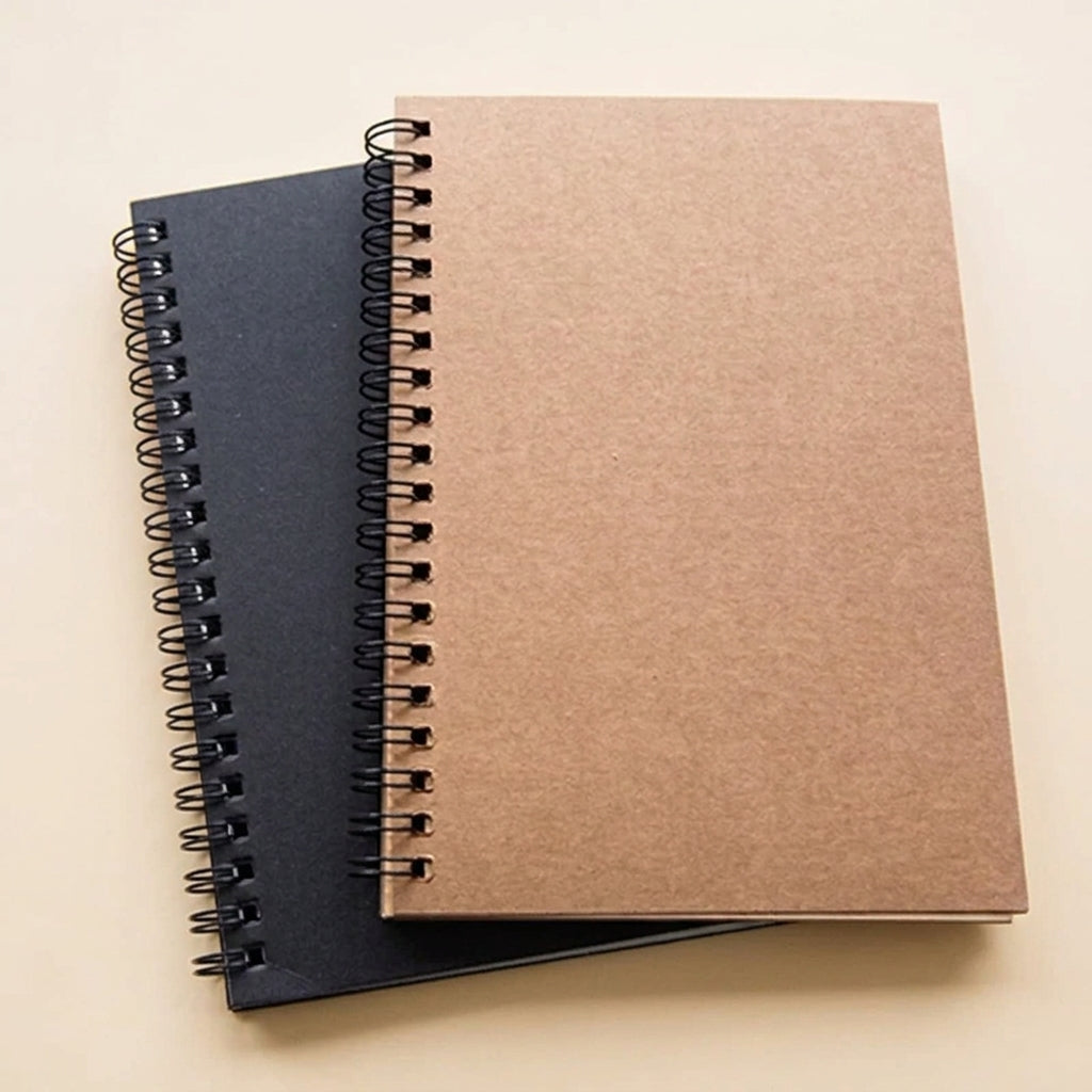 Two spiral-bound sketchpad on a light beige background, with one notebook in a brown kraft paper cover resting on top of another in a dark navy blue cover.