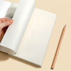 A hand holds the top corner of a blank white notebook, showing the clean interior pages. A wooden pencil rests to the right on a warm beige background.