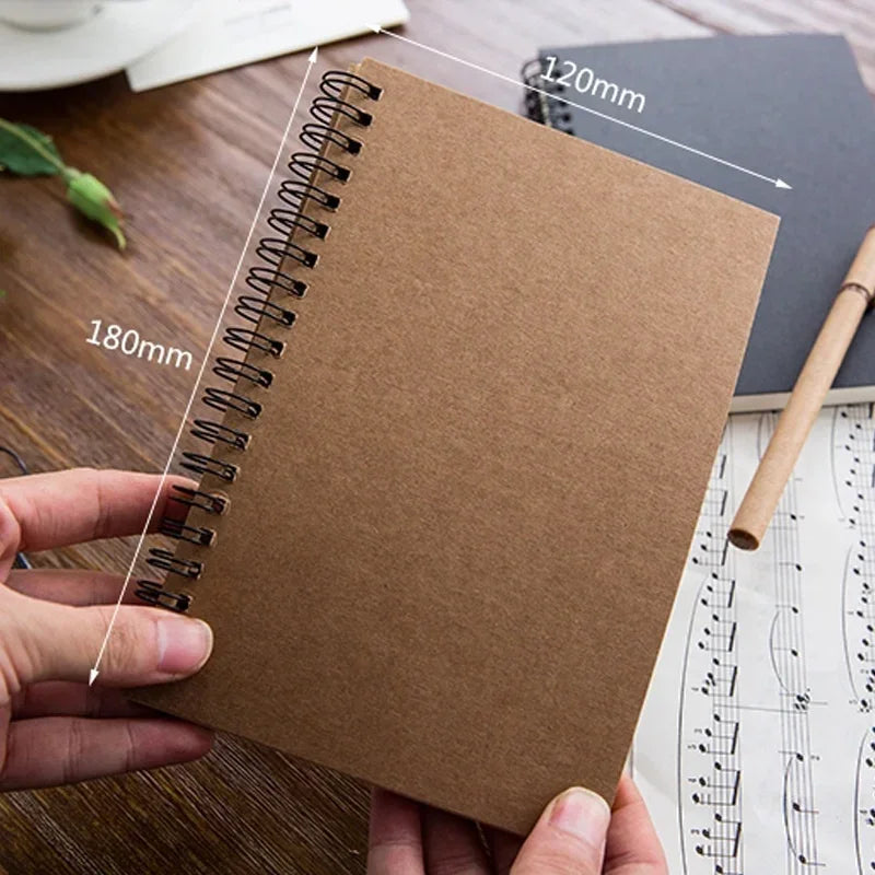 Brown spiral sketchpad held by a hand with measurements on a wooden surface.