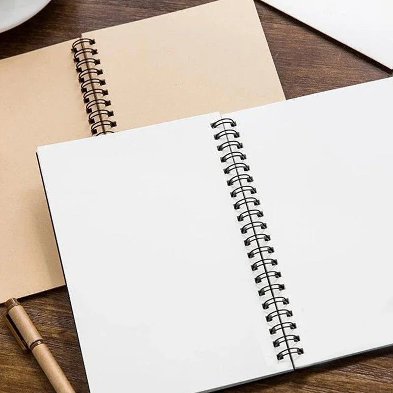 Open spiral-bound sketchpad on a wooden surface with a pen next to it.